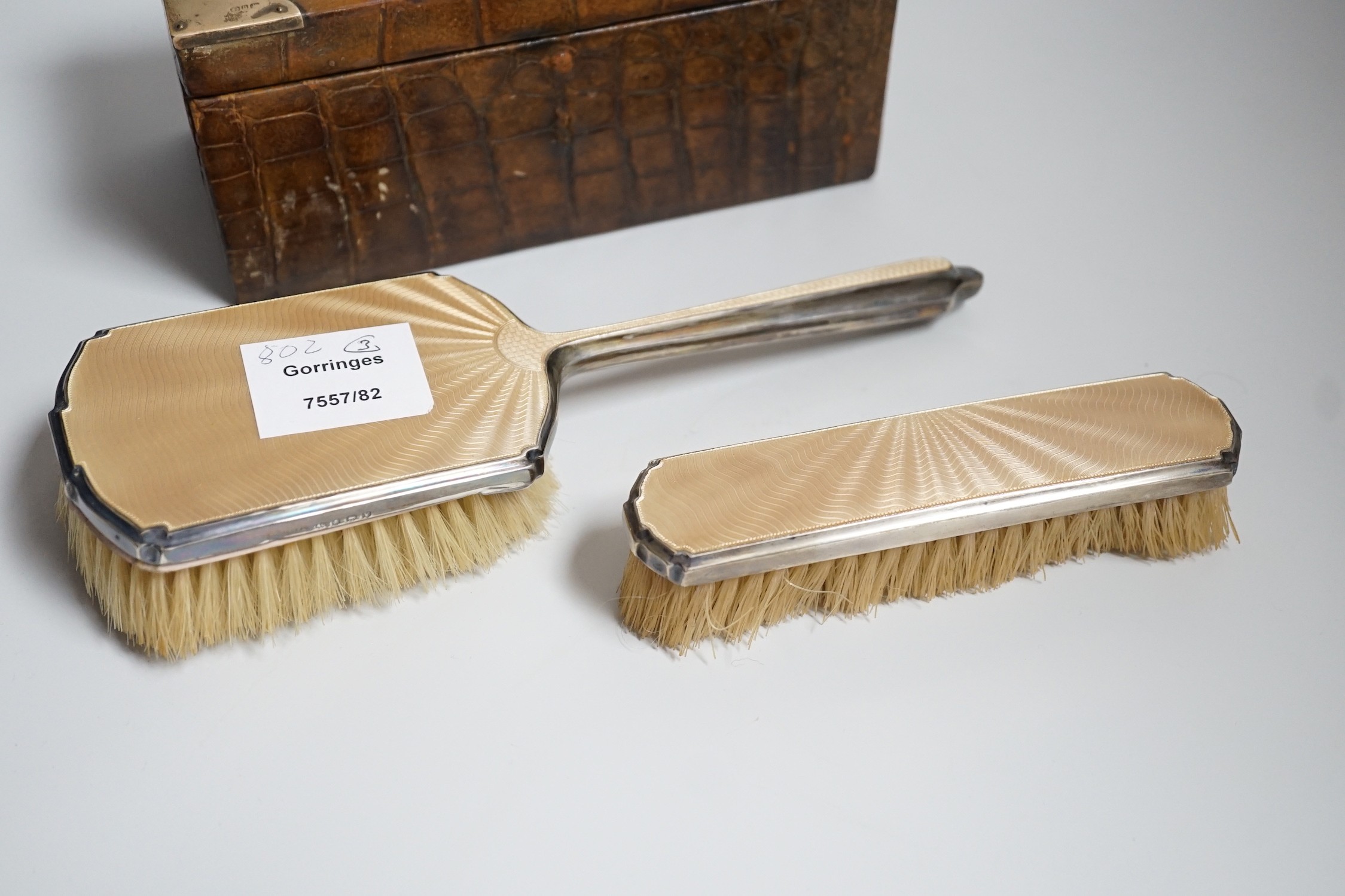 A late Victorian silver mounted crocodile skin jewellery box, 19cm and two silver and enamel mounted brushes.